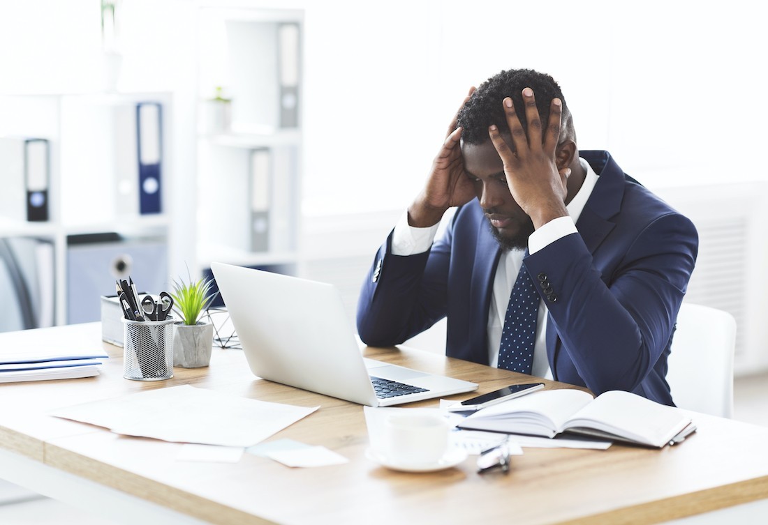 Stressed african-american young businessman sitting in office with hand on forehead