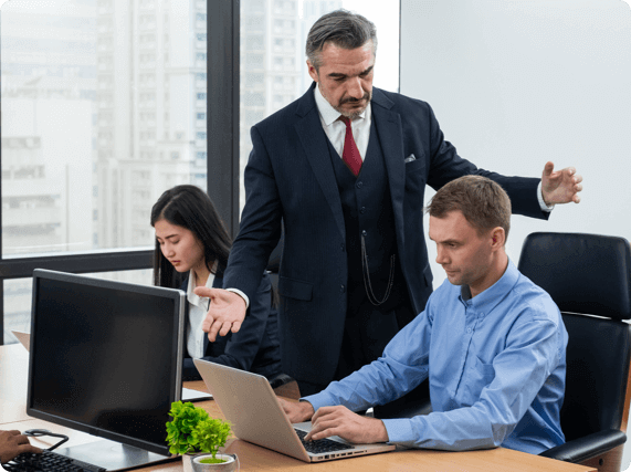 A boss standing over two stressed employees