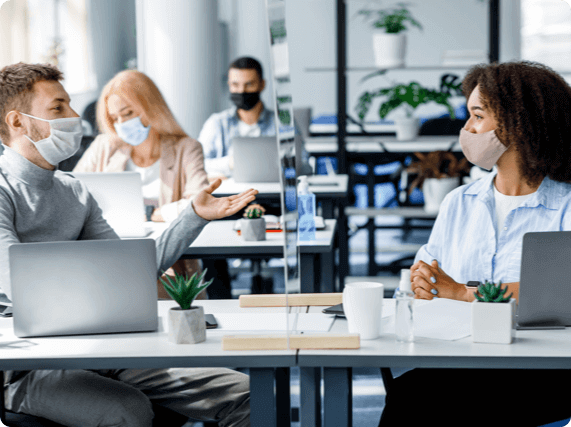 Two coworkers wearing masks separated by a plexiglass barrier