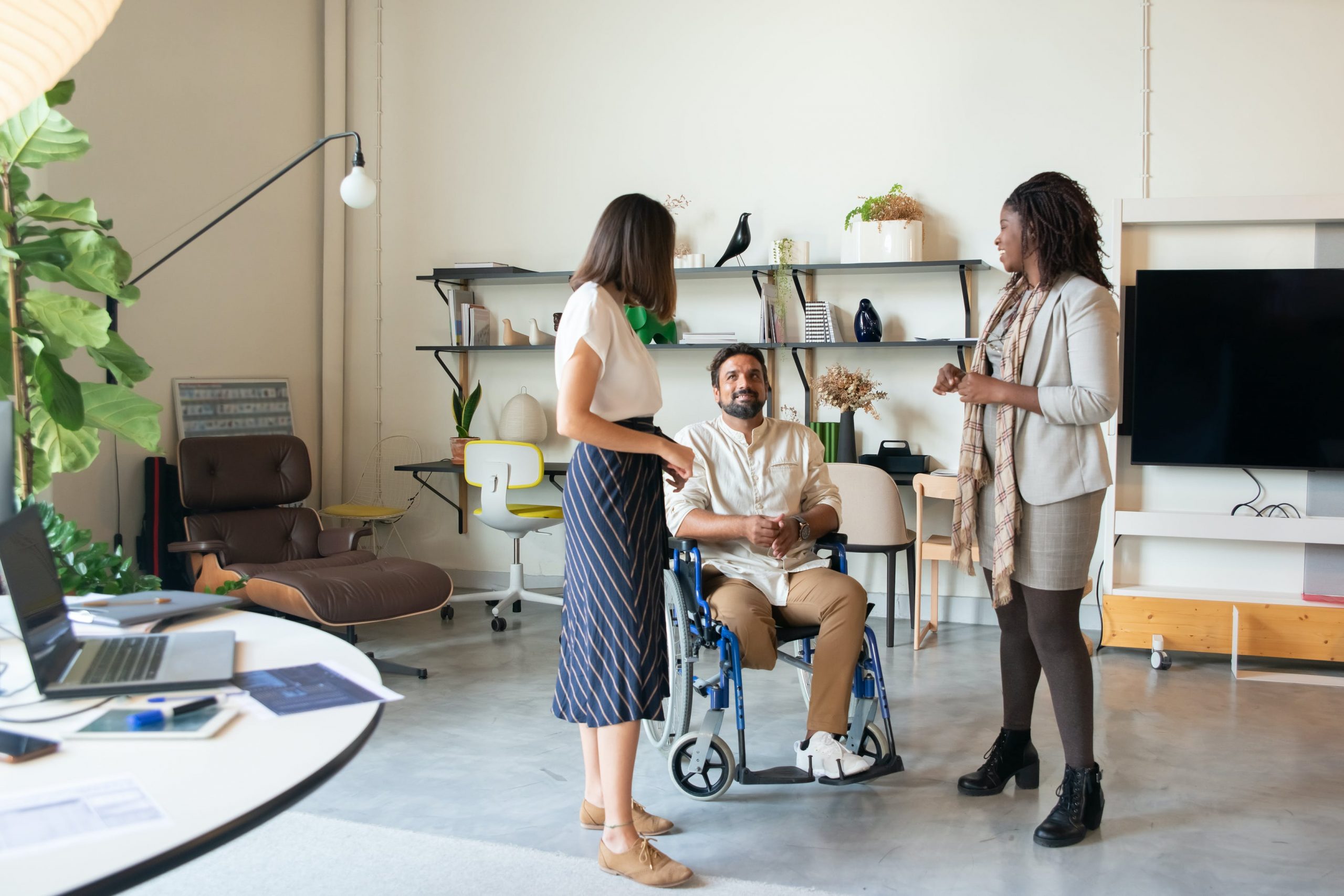 Caucasian women, disabled man, and black women stand in an office space discussing work