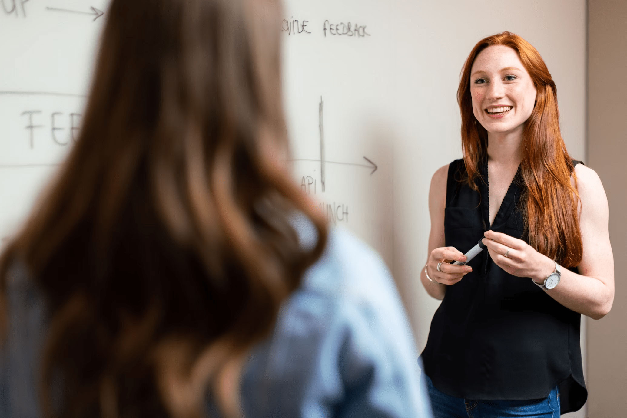 two women having a discussion in the office next to a white board