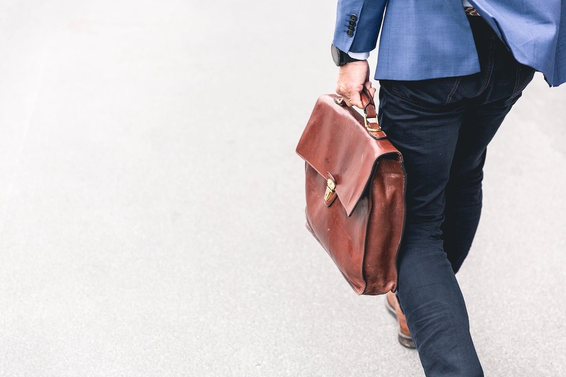 man in blue suit holding a brown briefcase walks to work