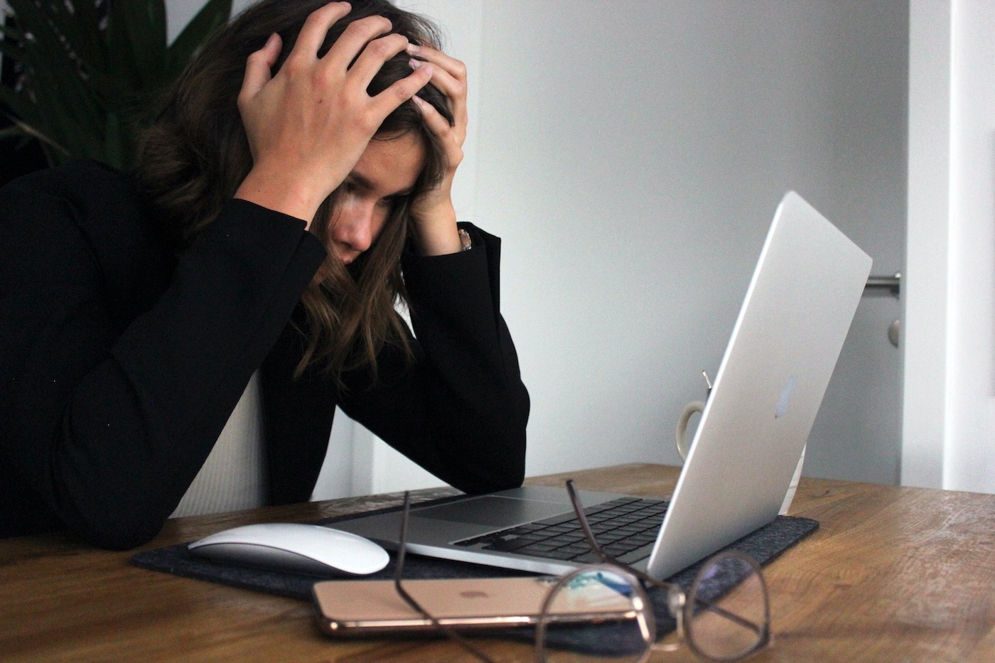 woman looking stressed holds her head in her hands while staring at a laptop computer at her desk