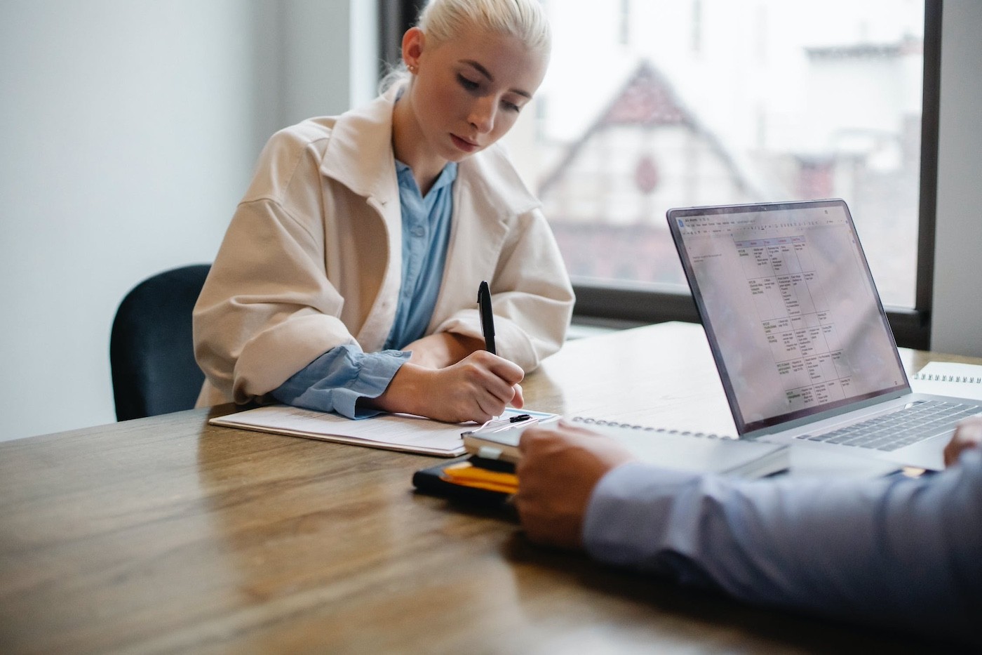 blonde woman sits across from man at a desk writing down notes