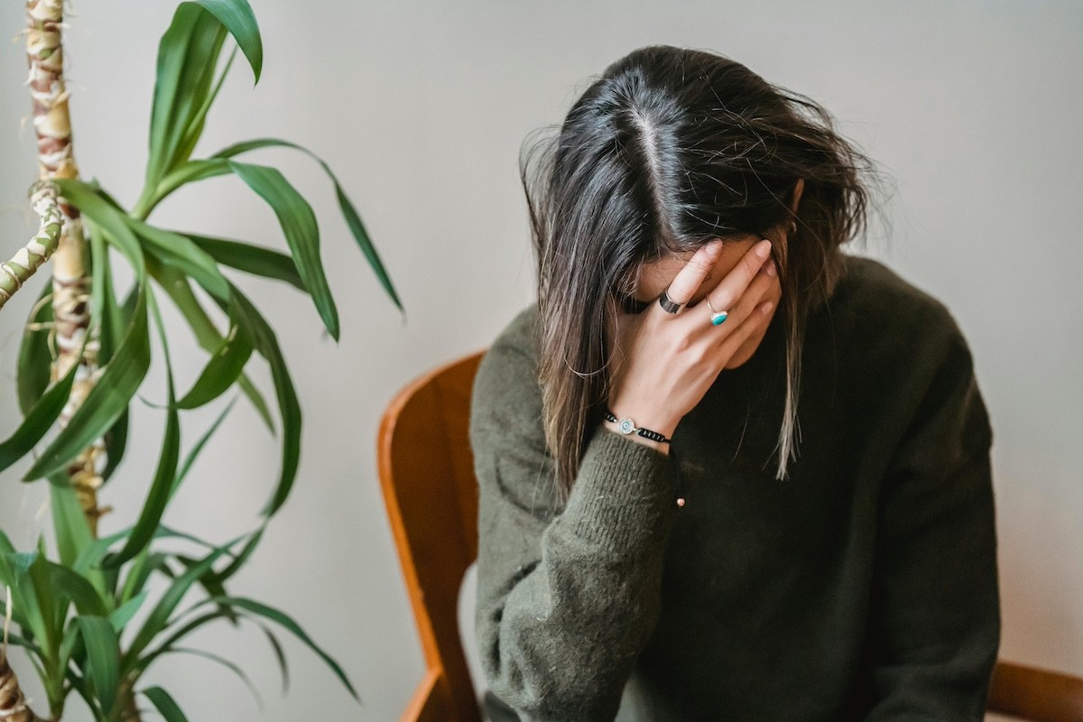 woman with dark hair and a dark green sweater holds her head in her hand