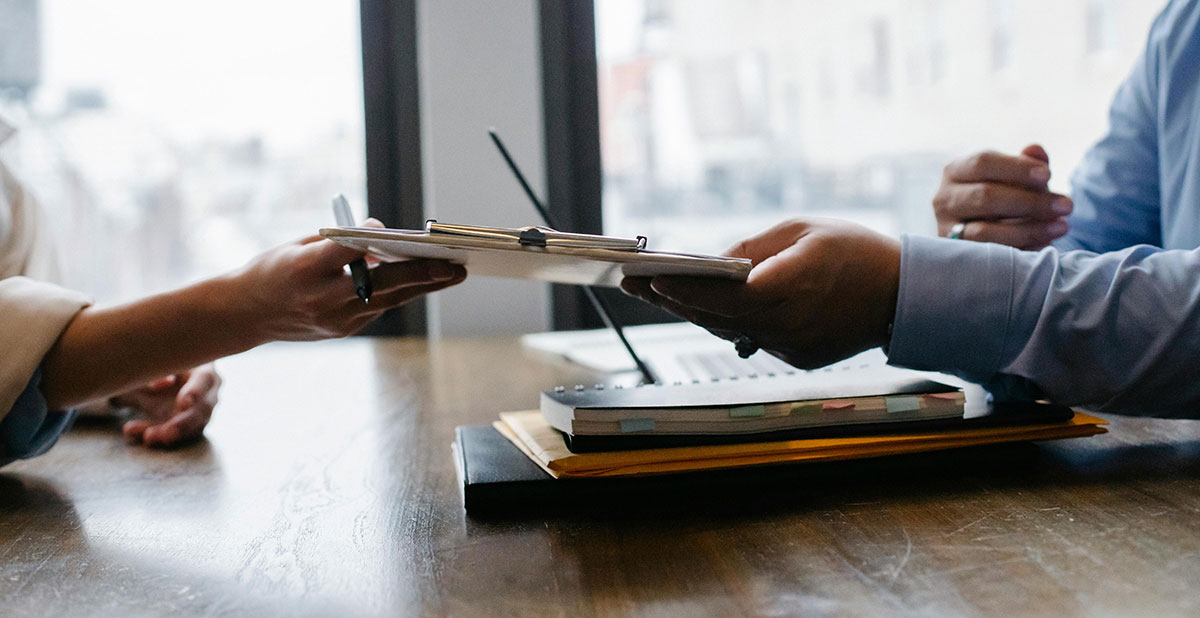 Two office workers pass a document across the table