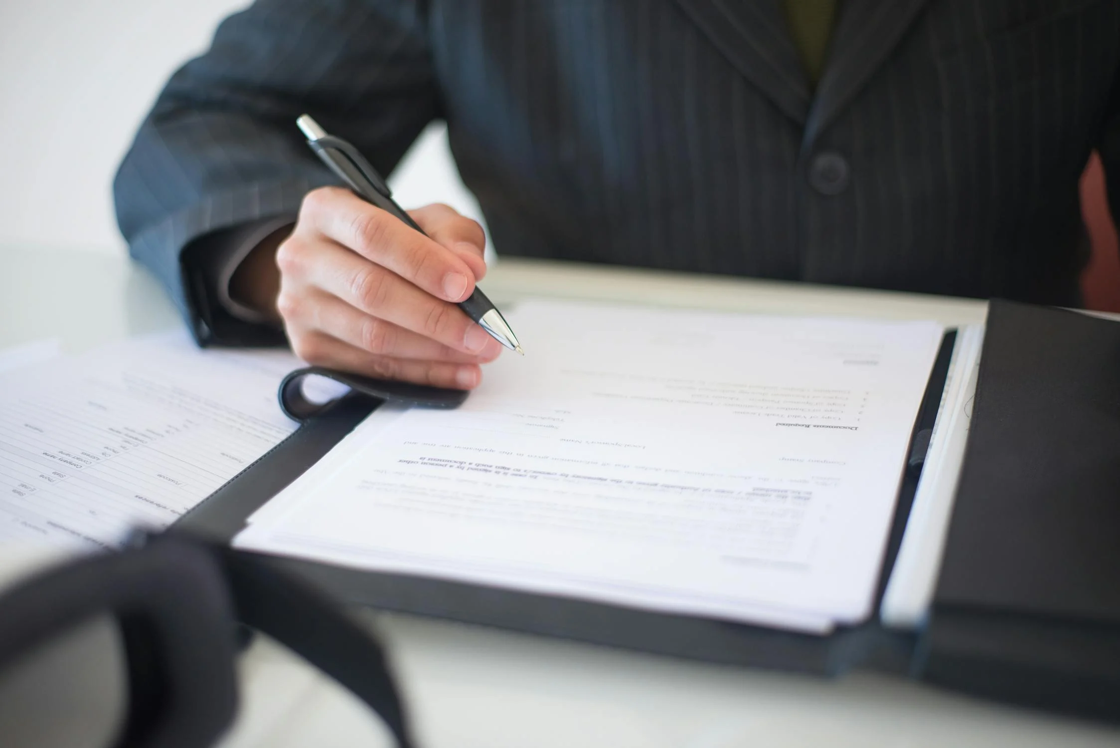 Man in a stripped suit signs legal documents at his desk