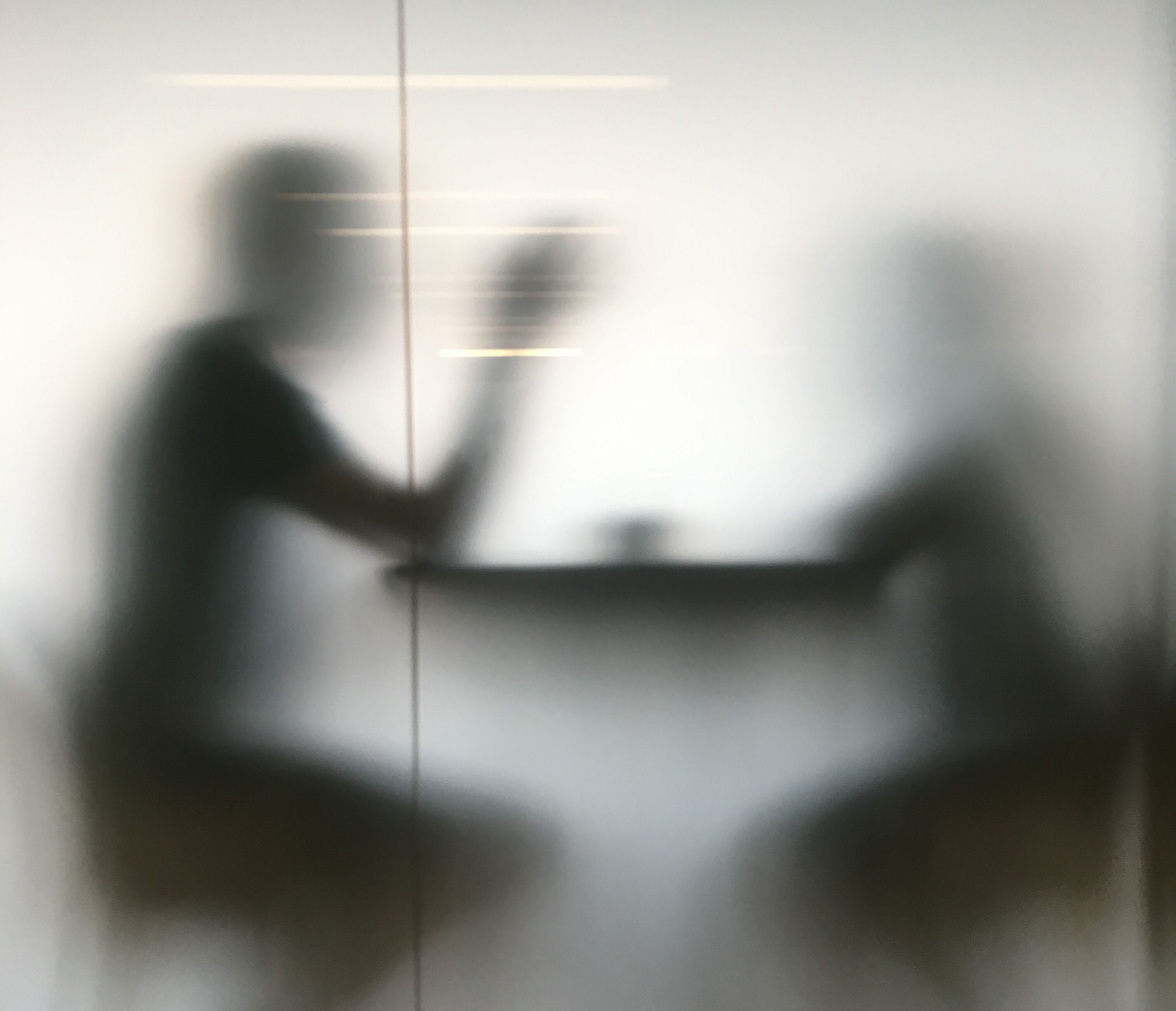blurry image of two individuals speaking at a table behind a glass window pane